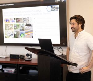 Person standing at podium speaking to a room with computer behind him.